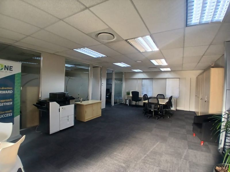 A functional open-plan office space featuring suspended ceilings, recessed lighting, glass partitions, and durable carpet tiles, suitable for a professional work environment.