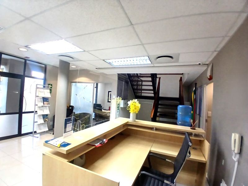 A professional office reception area featuring a built-in desk, glass partitions, tiled flooring, and a wooden staircase leading to the upper level.
