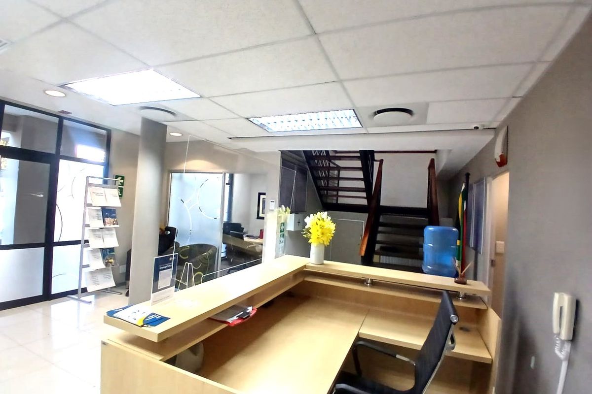 A professional office reception area featuring a built-in desk, glass partitions, tiled flooring, and a wooden staircase leading to the upper level.