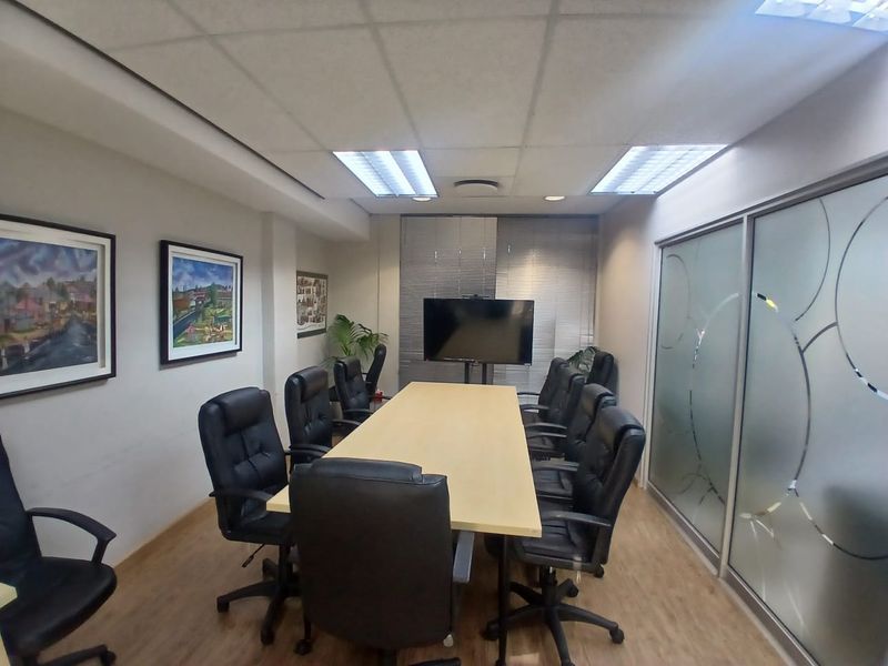 A professional office boardroom featuring a large meeting table, suspended ceiling with recessed lighting, and a modern frosted glass partition wall.