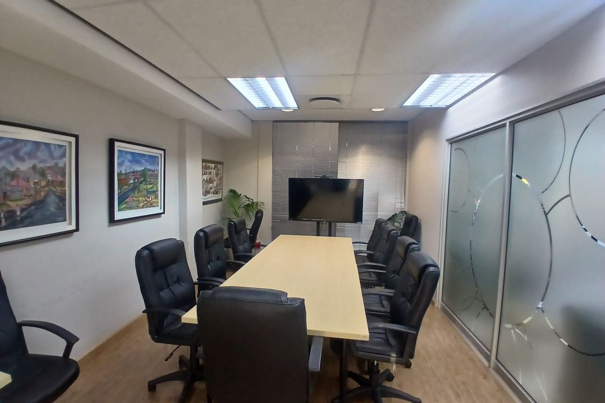 A professional office boardroom featuring a large meeting table, suspended ceiling with recessed lighting, and a modern frosted glass partition wall.