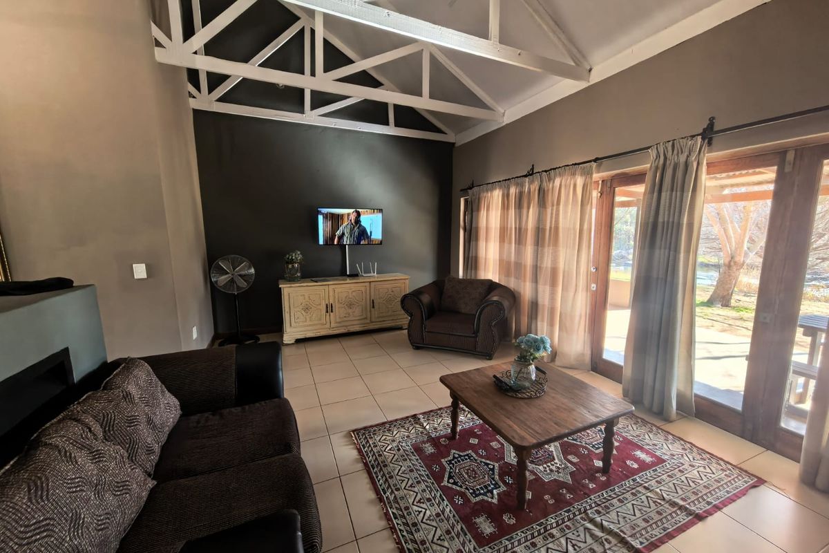 Spacious living room featuring high vaulted ceilings with exposed white timber trusses, tiled floors, and large glass sliding doors providing access to the patio.