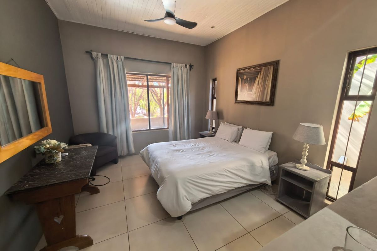 A well-maintained bedroom featuring tiled flooring, a timber-look ceiling with a fan, and large windows providing natural light.