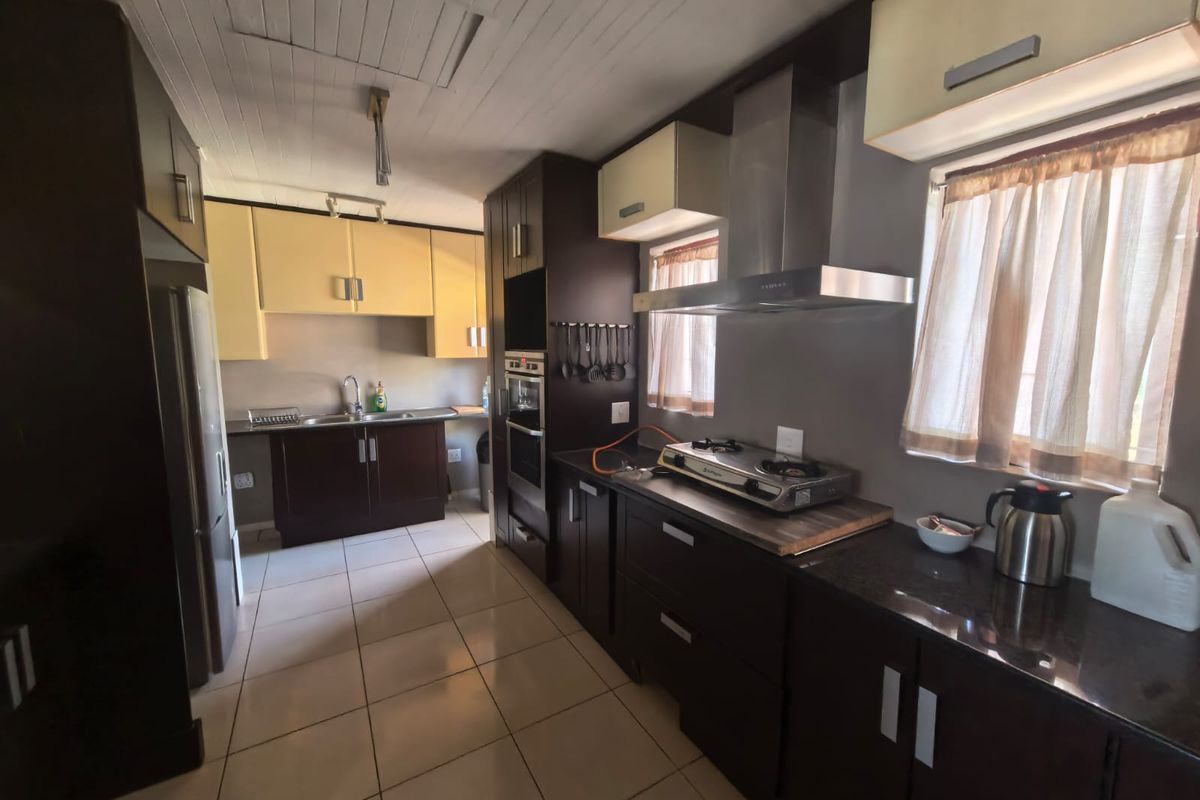 A functional kitchen featuring dark and light cabinetry, granite countertops, built-in oven, stainless steel extractor fan, and tiled flooring.