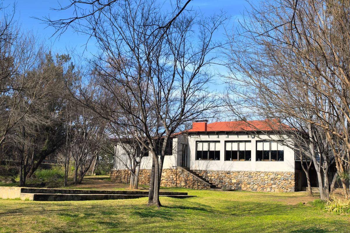 Rear view of a business property featuring stone cladding, a tiled roof, and large windows set within a spacious, tree-lined garden area.