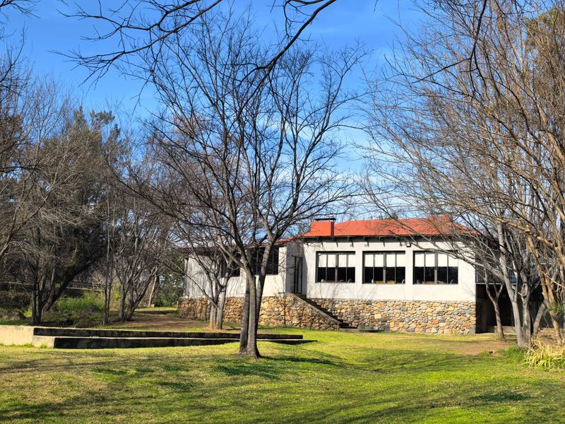 Rear view of a business property featuring stone cladding, a tiled roof, and large windows set within a spacious, tree-lined garden area.