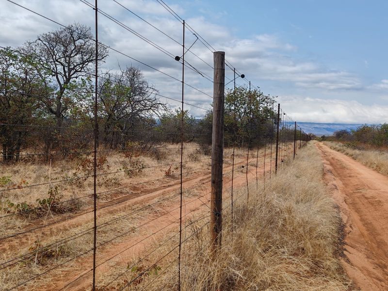 A view of a rural farm boundary featuring wire fencing with timber posts running alongside a dirt track in a natural landscape.