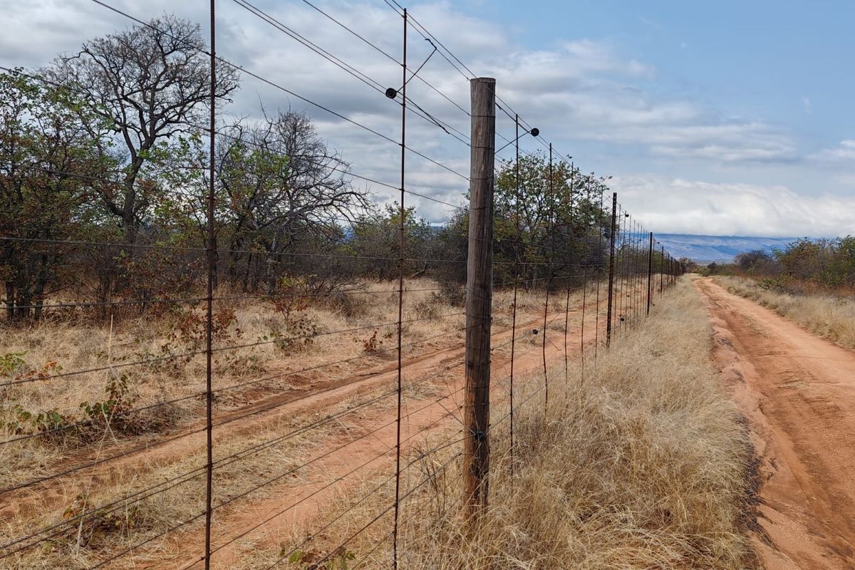 A view of a rural farm boundary featuring wire fencing with timber posts running alongside a dirt track in a natural landscape.