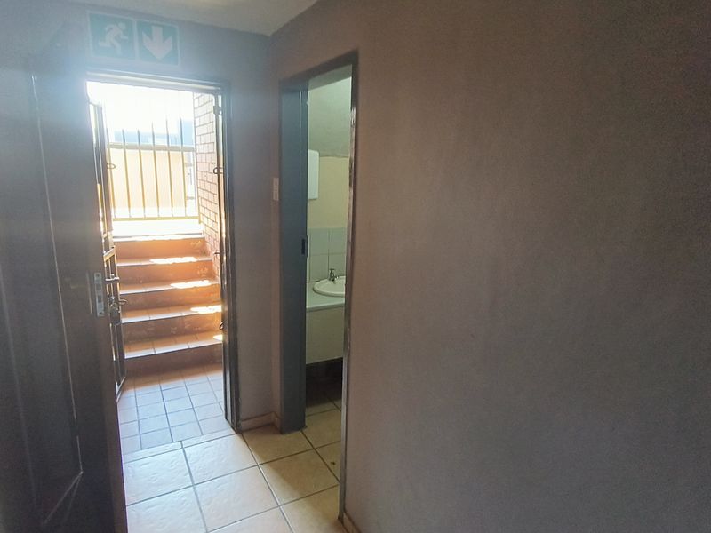 A functional hallway area featuring tiled flooring, an emergency exit leading to external stairs, and access to a small washroom with a basin.