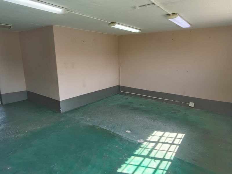 An empty utility space featuring painted concrete flooring, fluorescent lighting, and a glass block window, suitable for various industrial or storage purposes.