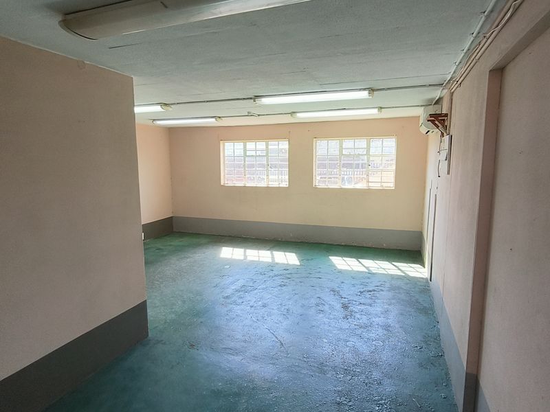 An open-plan industrial utility space featuring painted concrete floors, fluorescent lighting, and wall-mounted air conditioning, suitable for storage or workshop use.