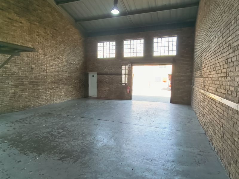 Spacious industrial utility area featuring exposed brick walls, high ceilings, concrete flooring, and a large roller shutter door for easy access.