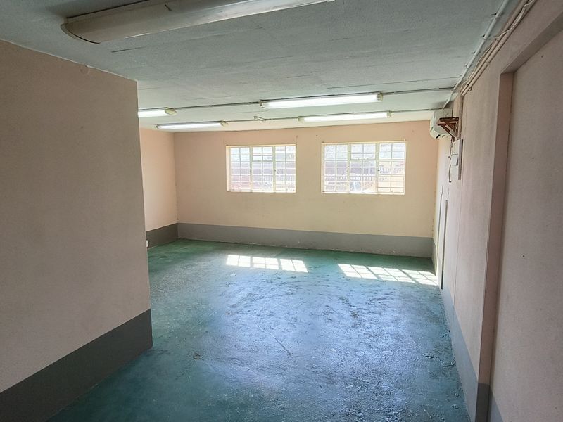 An open-plan industrial utility space featuring painted concrete flooring, fluorescent lighting, and steel-framed windows, suitable for storage or workshop use.