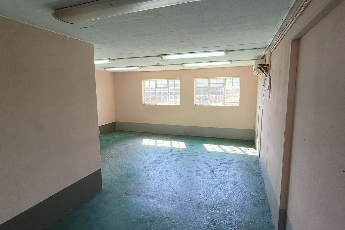 An open-plan industrial utility space featuring painted concrete flooring, fluorescent lighting, and steel-framed windows, suitable for storage or workshop use.