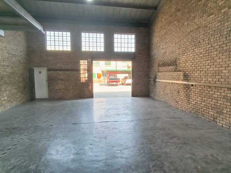 Spacious industrial warehouse or garage unit featuring exposed brick walls, durable concrete flooring, and high ceilings with natural light from industrial windows.