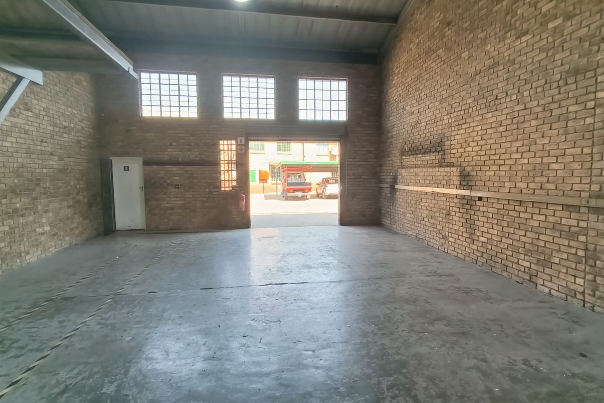 Spacious industrial warehouse or garage unit featuring exposed brick walls, durable concrete flooring, and high ceilings with natural light from industrial windows.