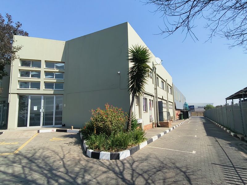 Exterior view of an industrial property featuring a paved driveway, secure perimeter fencing, and a multi-level building facade with large windows.