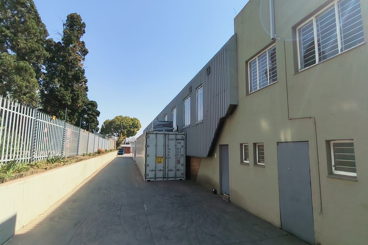 Rear exterior view of the industrial property featuring a paved driveway, secure metal fencing, and corrugated metal cladding on the building facade.
