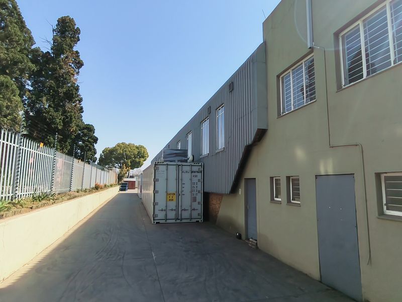 Rear exterior view of the industrial property featuring a paved driveway, secure metal fencing, and corrugated metal cladding on the building facade.
