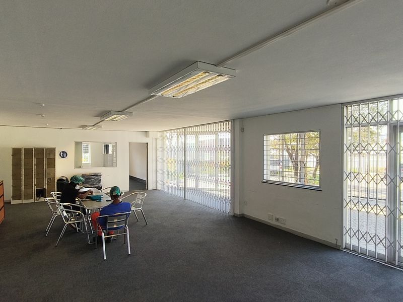 Open-plan office space featuring carpeted flooring, fluorescent lighting, and secure metal security gates and window bars.