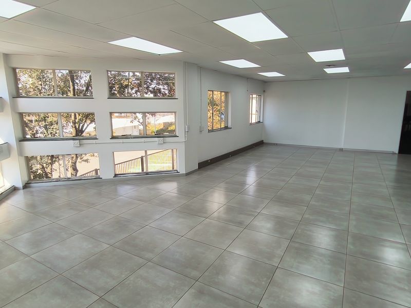 Spacious, open-plan office area featuring modern tiled flooring, a suspended ceiling with recessed lighting, and large windows providing ample natural light.