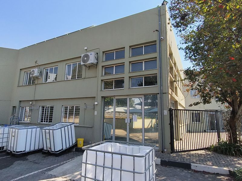 Exterior view of an industrial building featuring a paved entrance area, security gates, and multiple wall-mounted air conditioning units.