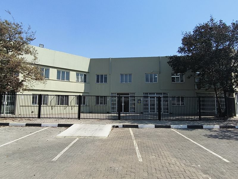 Front exterior view of an industrial building featuring a paved parking area, security fencing, and gated access.