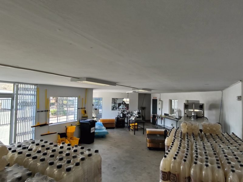 A functional industrial utility space featuring concrete flooring, fluorescent lighting, and secure access points, currently utilized for storage and light production activities.