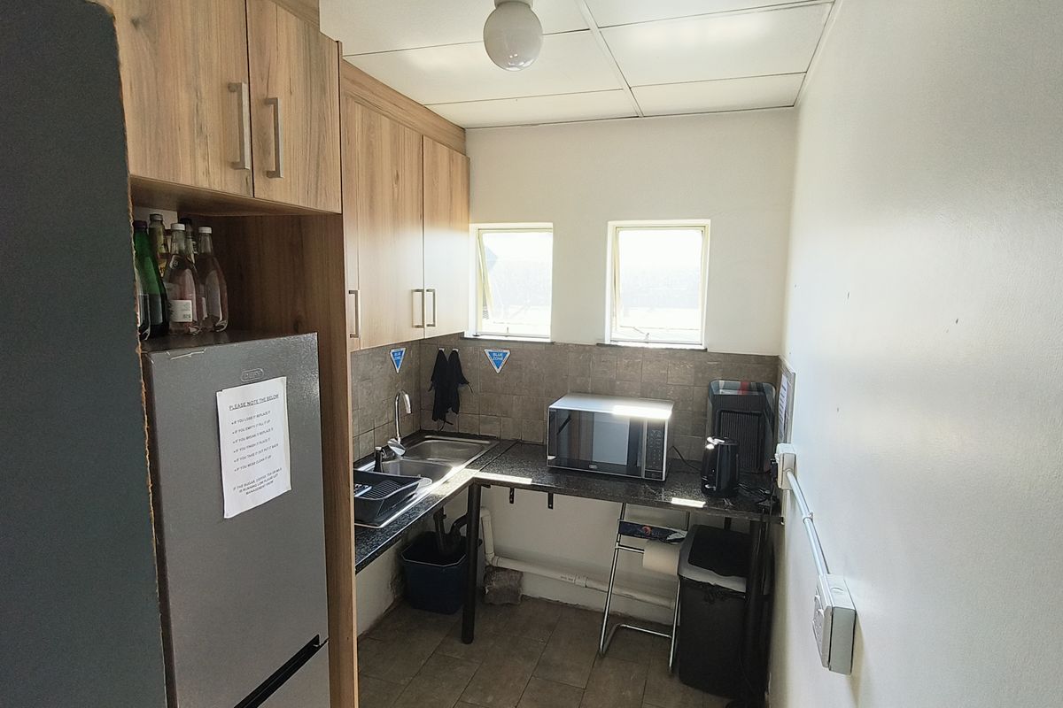 Compact industrial kitchen area featuring laminate cabinetry, stone countertops, a stainless steel sink, and tiled backsplash with functional overhead lighting.