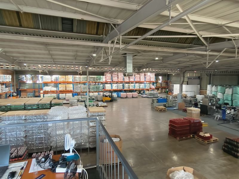 Spacious industrial warehouse facility featuring high ceilings with steel trusses, concrete flooring, and extensive integrated racking systems for storage and manufacturing operations.