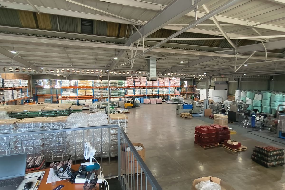 Spacious industrial warehouse facility featuring high ceilings with steel trusses, concrete flooring, and extensive integrated racking systems for storage and manufacturing operations.