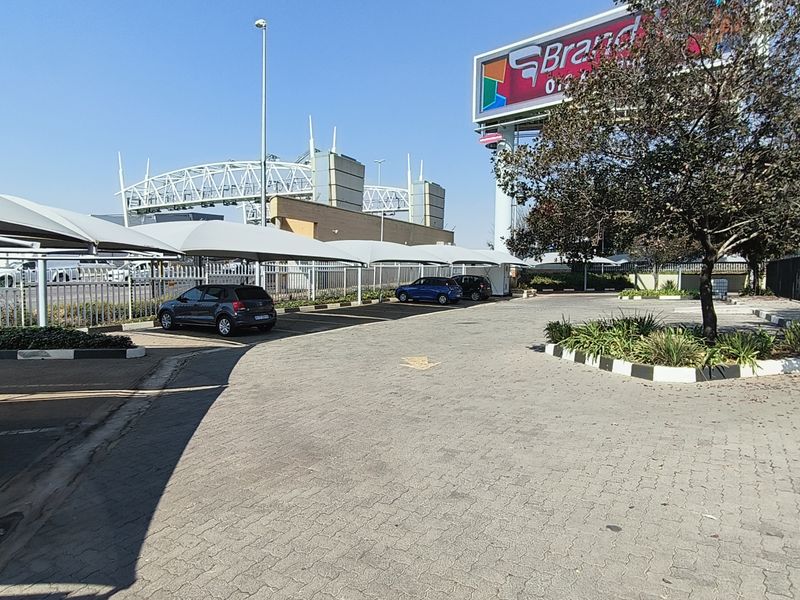 Industrial property exterior featuring a paved parking area with shade cloth carports, security fencing, and a prominent advertising billboard.