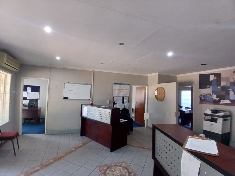 A functional office reception area featuring tiled flooring, recessed lighting, and a built-in reception desk, providing a professional entry point for the workspace.