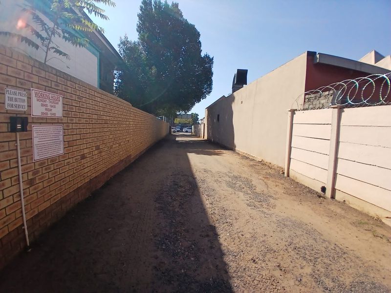 A narrow, unpaved rear access driveway enclosed by brick and precast concrete boundary walls with security razor wire.