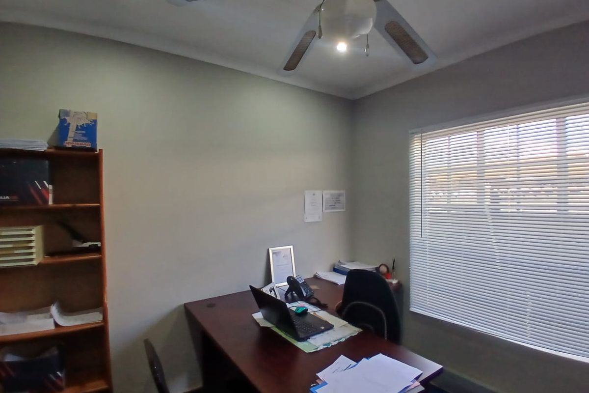 A functional office space featuring a ceiling fan, venetian blinds, and recessed lighting, providing a practical environment for professional work.