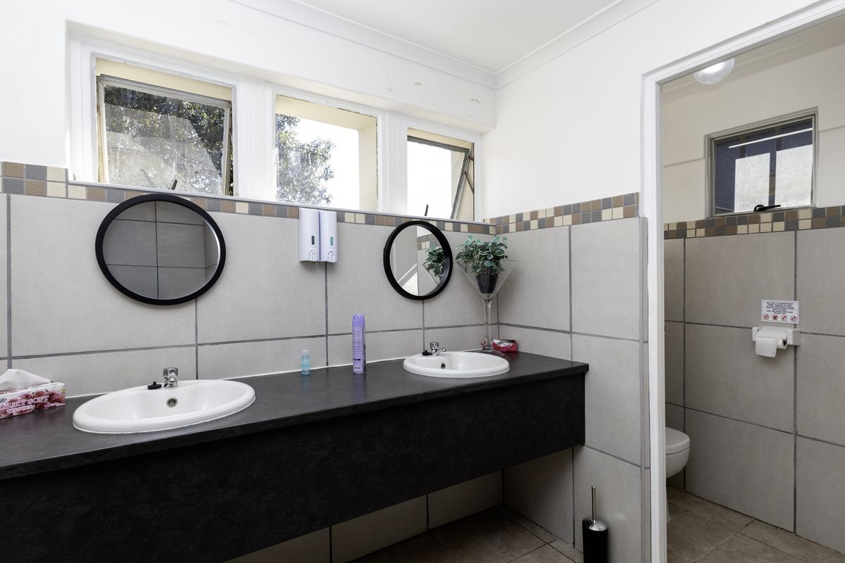 A functional restaurant restroom featuring a dual vanity with integrated basins, tiled splashbacks, and a separate toilet cubicle with natural light.
