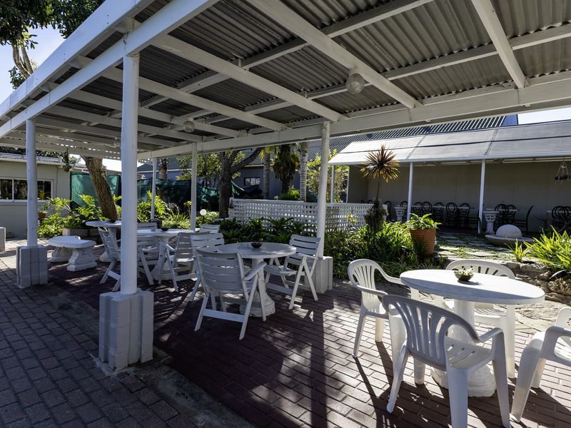 A covered outdoor patio area featuring brick paving, a corrugated metal roof structure, and established garden landscaping, suitable for restaurant outdoor seating.