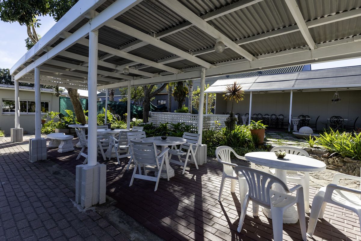 A covered outdoor patio area featuring brick paving, a corrugated metal roof structure, and established garden landscaping, suitable for restaurant outdoor seating.