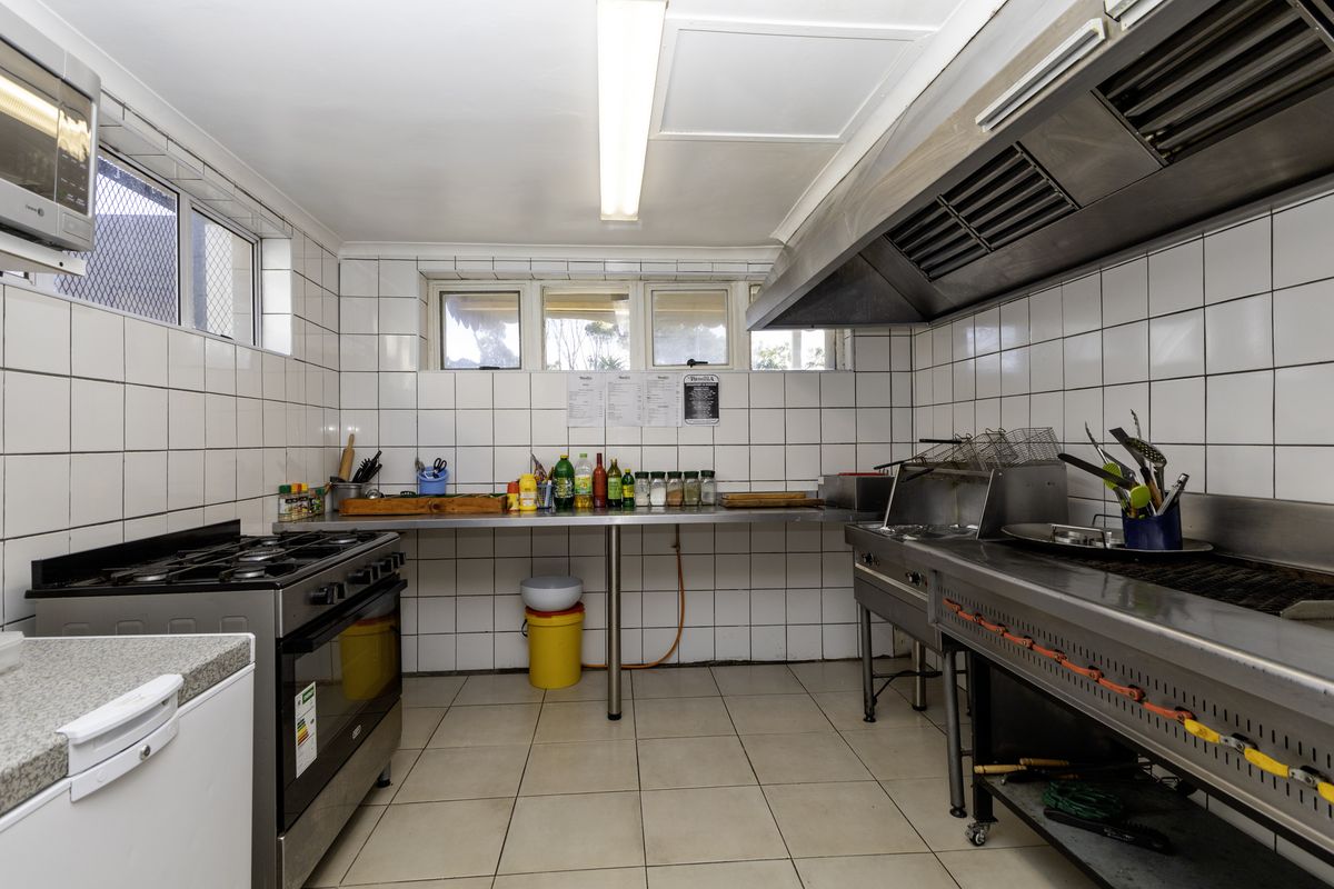 A functional commercial kitchen featuring stainless steel prep counters, a large extractor hood, commercial-grade gas cooking equipment, and durable tiled finishes throughout.