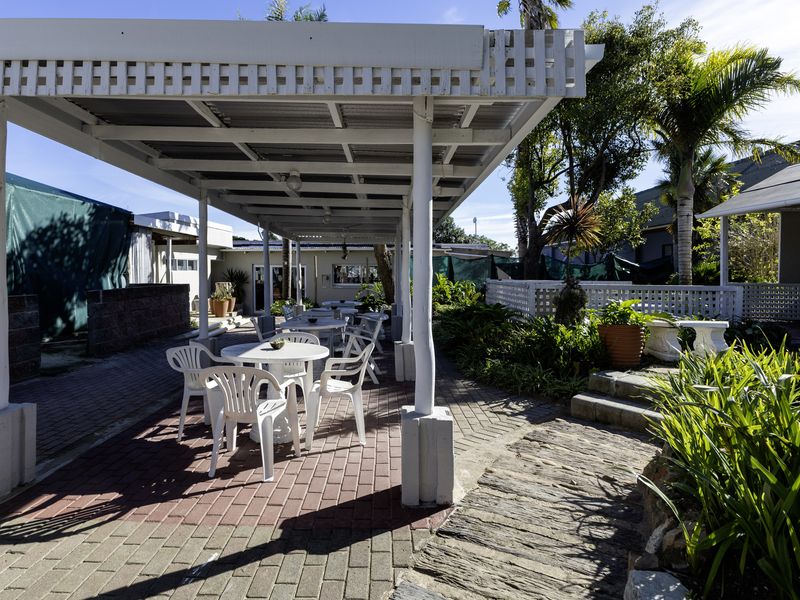 Outdoor patio area featuring a covered pergola structure with paved flooring and landscaped garden borders, suitable for restaurant dining.