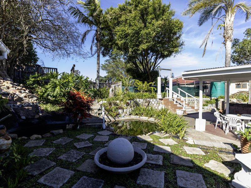 A landscaped garden area featuring stone paving, a water feature, a retaining wall, and a covered patio space.