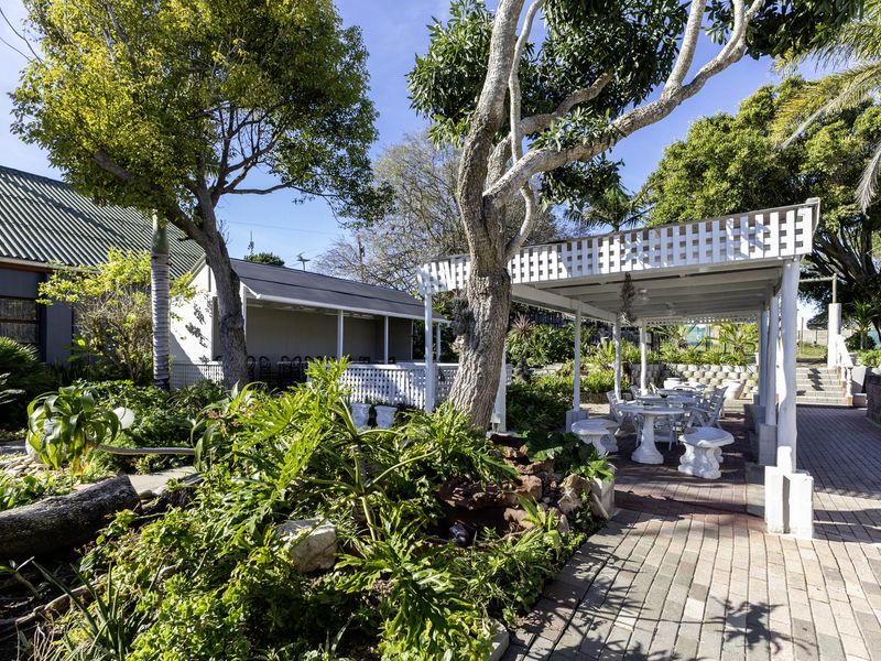 A well-maintained outdoor patio area featuring a white pergola, paved walkways, and established garden landscaping, ideal for restaurant outdoor dining.
