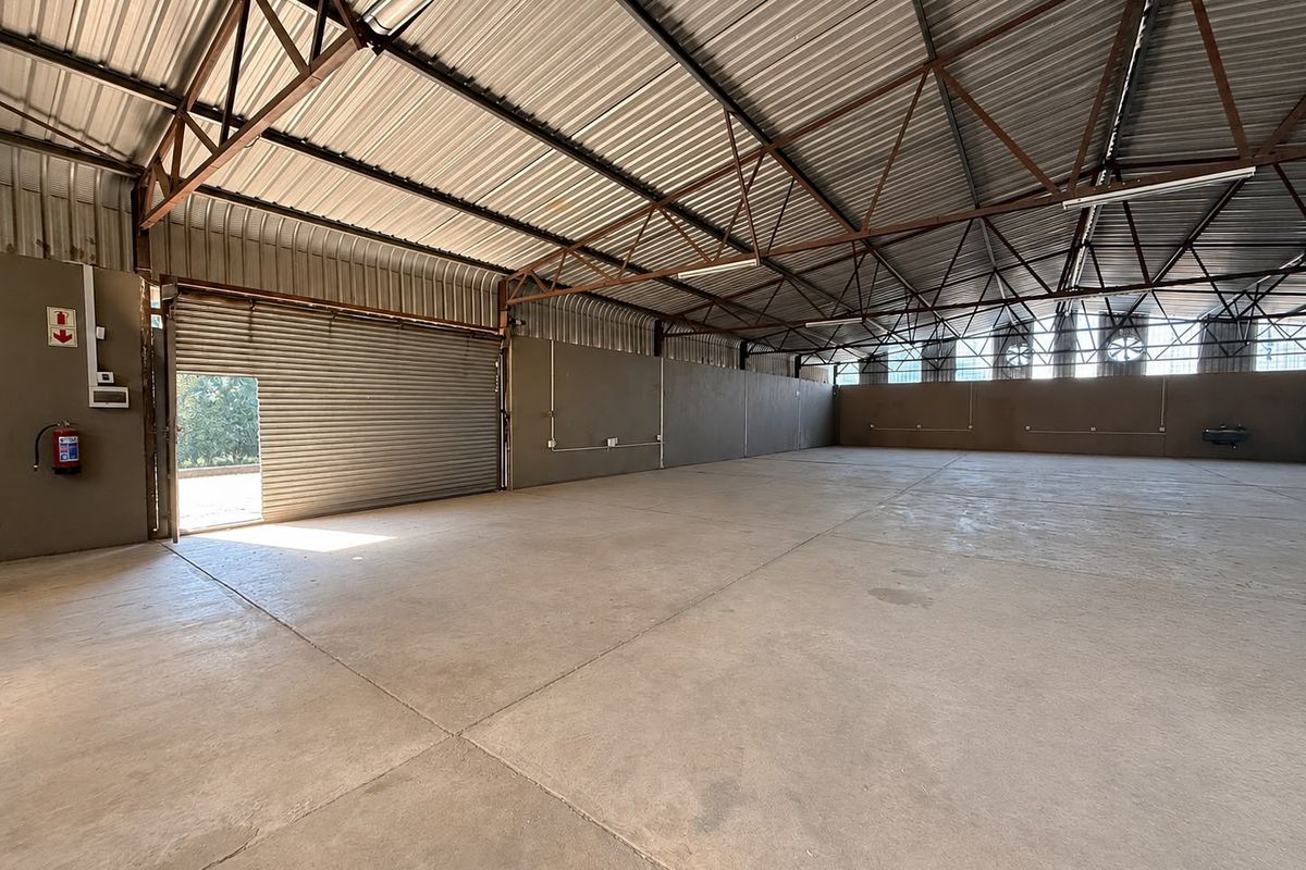 Spacious industrial warehouse unit featuring concrete flooring, high-clearance metal roof structure, and a large roller shutter door for easy access.