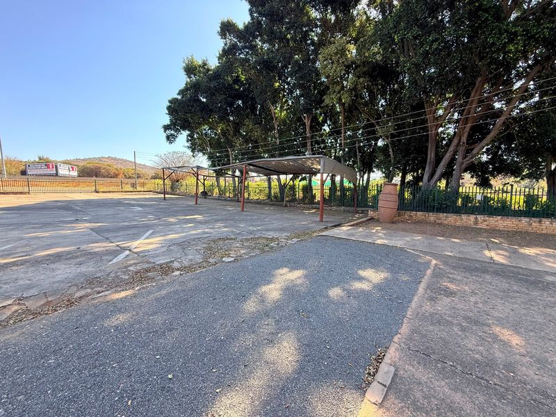 Industrial outdoor parking area featuring concrete paving, shade cloth carports, and secure perimeter fencing with mature trees.
