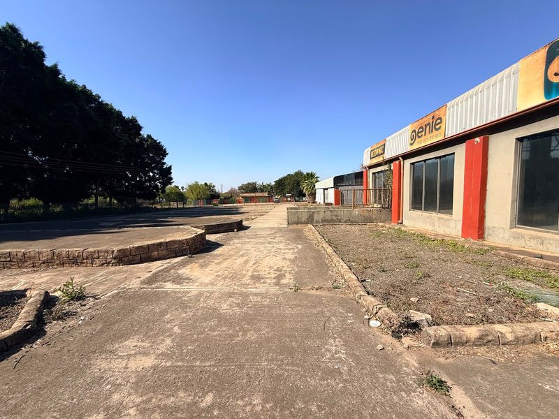 Industrial property exterior featuring a large concrete driveway, retaining walls, and commercial building facade with display windows.