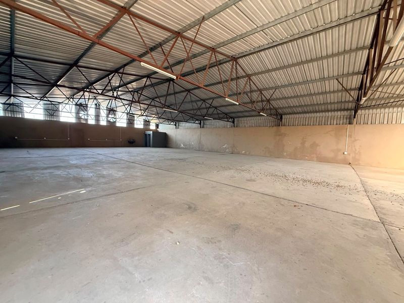 Spacious industrial warehouse unit featuring high-clearance exposed steel trusses, concrete flooring, and natural light from high-level windows.