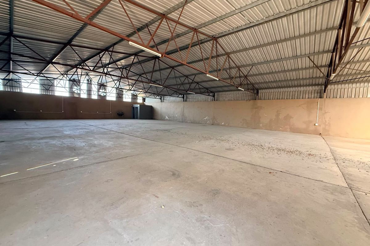 Spacious industrial warehouse unit featuring high-clearance exposed steel trusses, concrete flooring, and natural light from high-level windows.