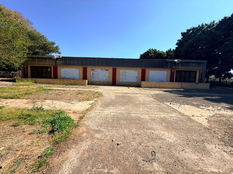 Front view of an industrial property featuring a large concrete driveway, metal roofing, and multiple access points with security gates.