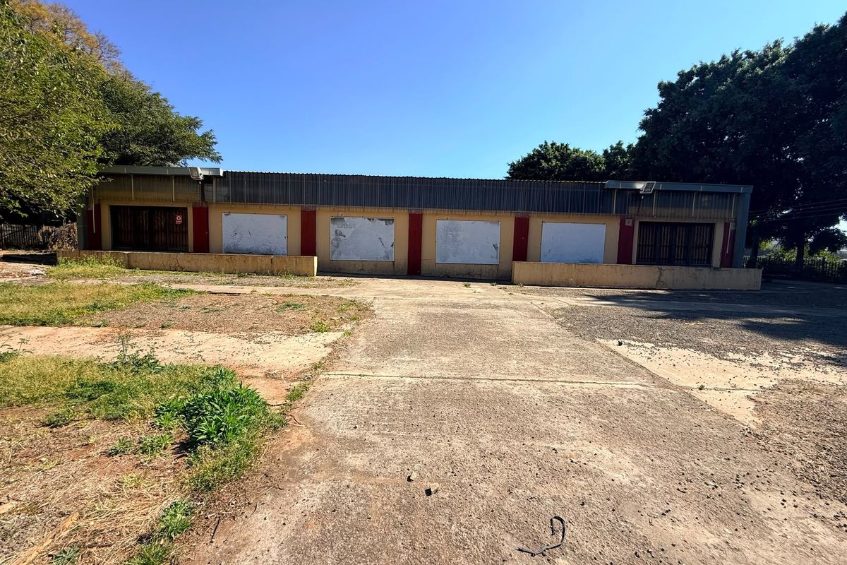 Front view of an industrial property featuring a large concrete driveway, metal roofing, and multiple access points with security gates.