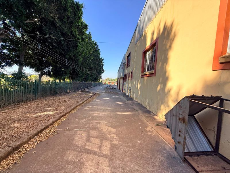 Exterior side view of an industrial property featuring concrete paving, security fencing, and a painted facade with window security bars.